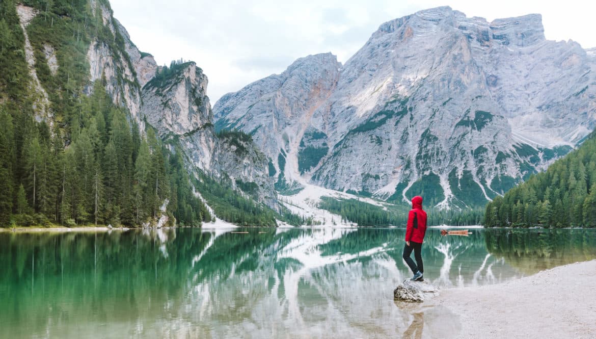 a person standing on a rock in front of a mountain lake.