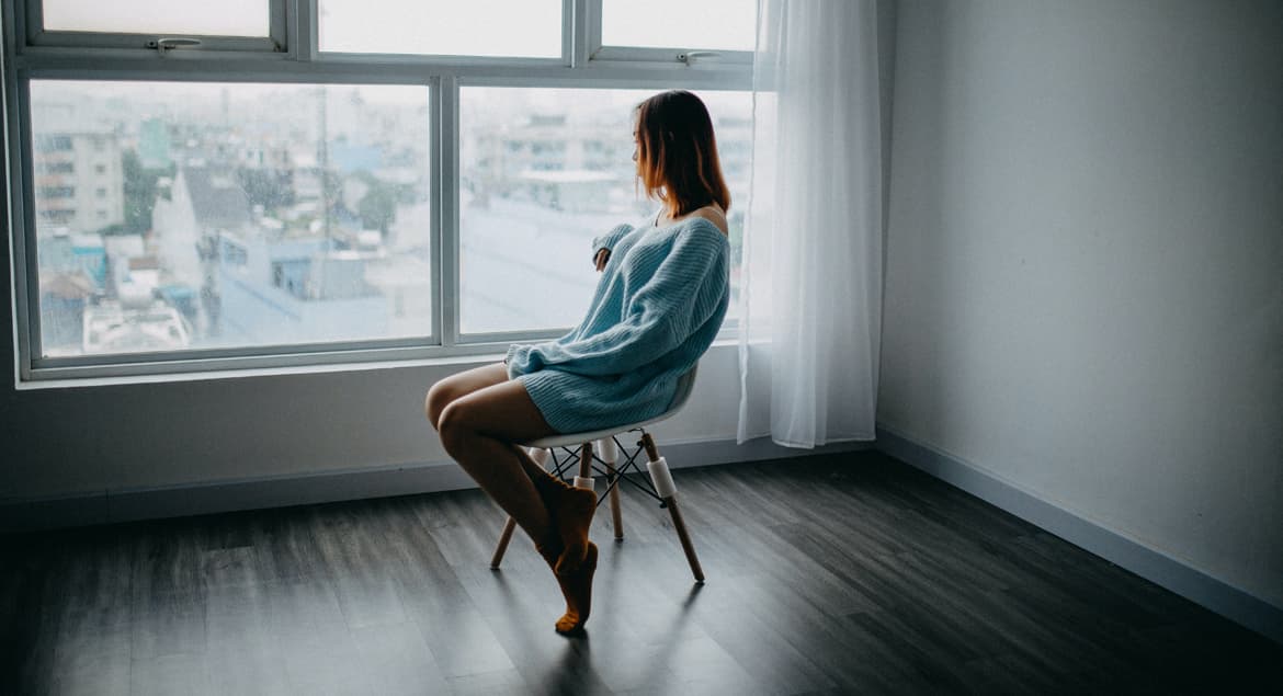 A woman sitting in a chair looking out a window after relocation.