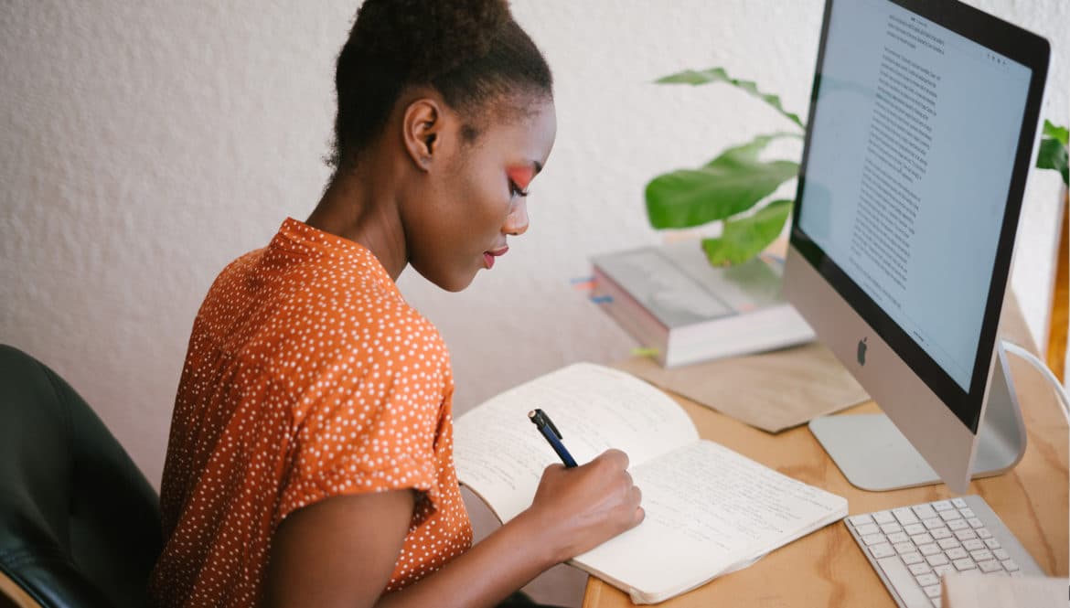 A woman using freelance tools to write in a notebook on her desk.