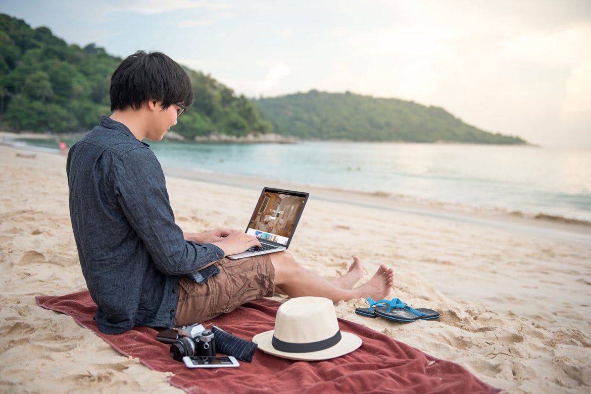 A digital nomad on a beach using a laptop computer.