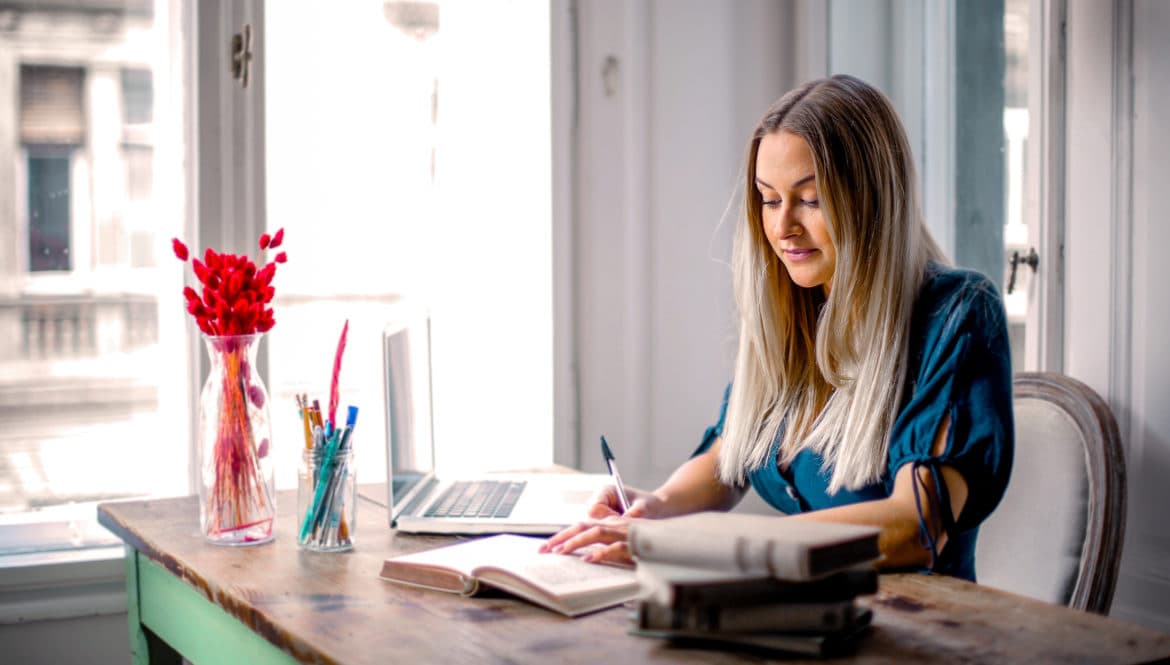 a woman sitting at a table with a book and a laptop.
