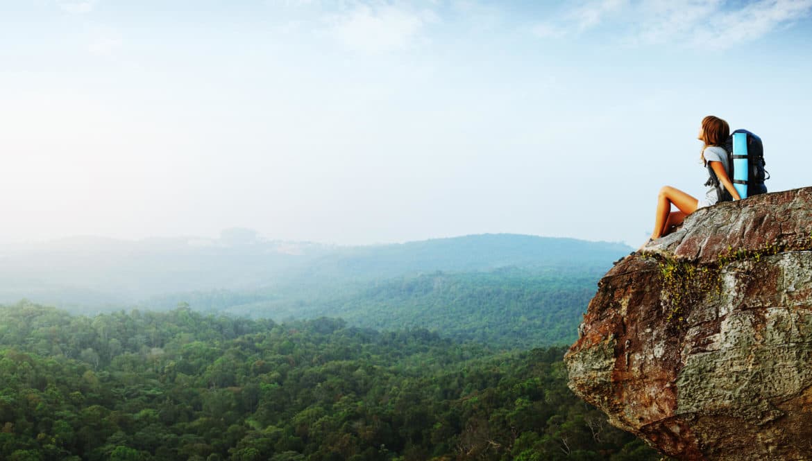 A person practicing slow travel sitting on top of a cliff.