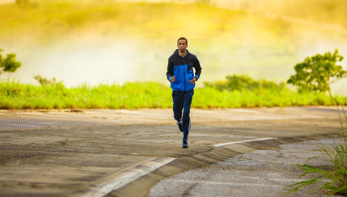A fitness enthusiast running down a road in a blue jacket.