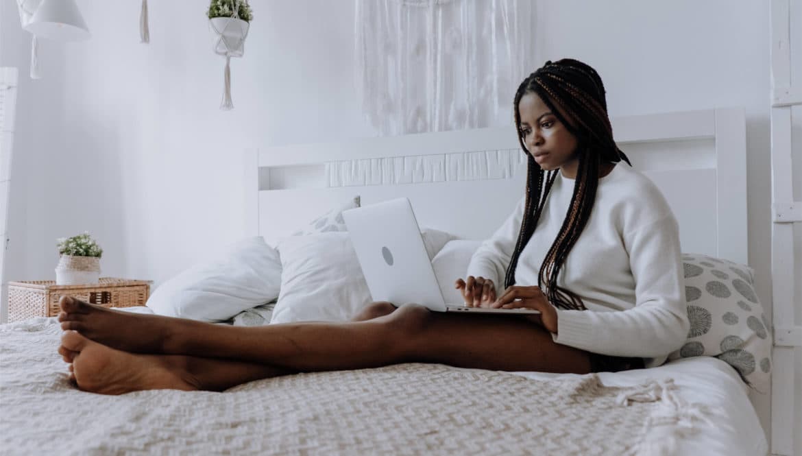 a woman sitting on a bed using a laptop computer.