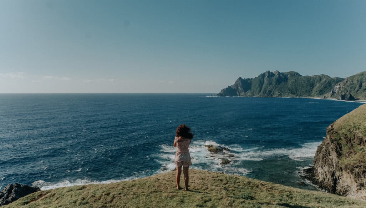 A digital nomad enjoying the Philippines, standing on top of a lush green hillside next to the ocean.