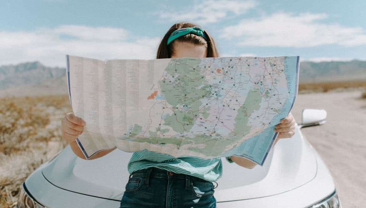 a woman holding a map in front of a car.