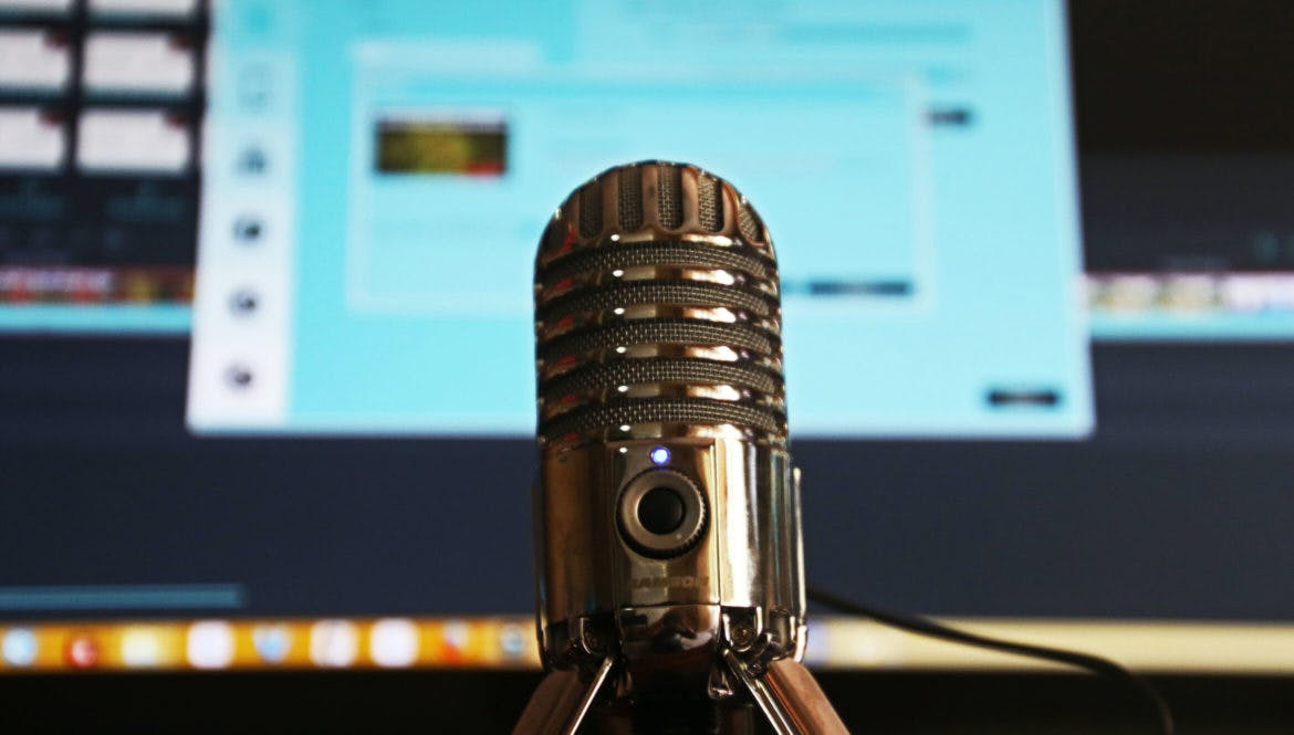 A microphone for remote work sitting in front of a computer monitor.