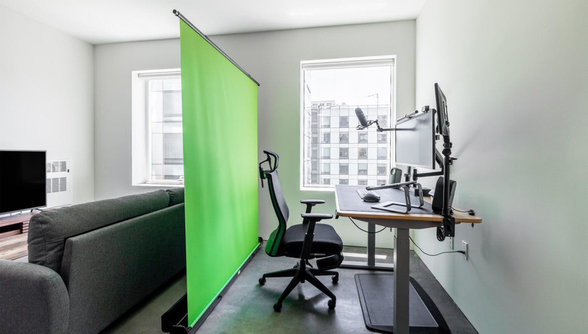 A rental living room with a green screen in the corner for remote work.
