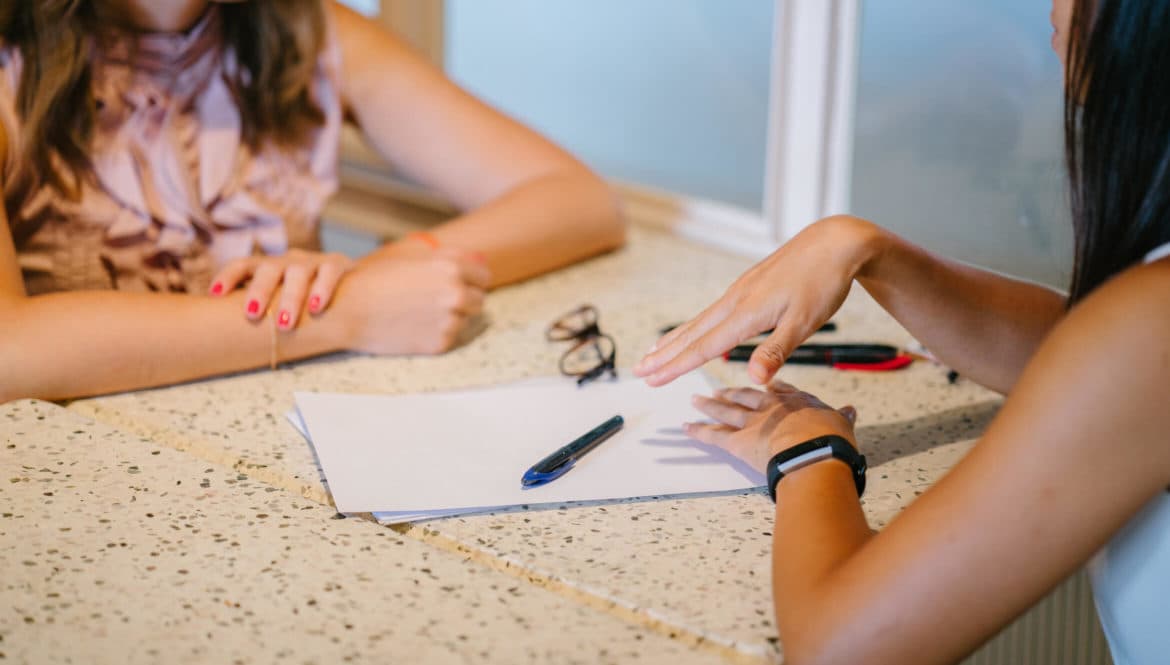 Two women writing about how to put remote work on the resume at a table.