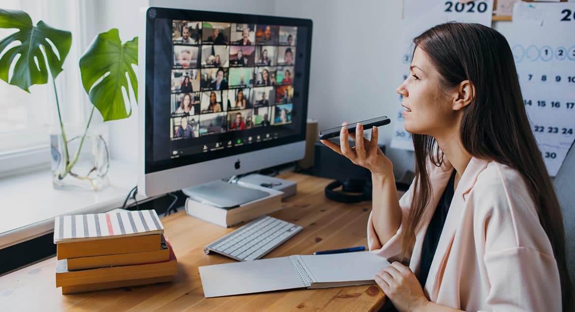 A woman managing a remote team sits at her computer with a pen in hand.