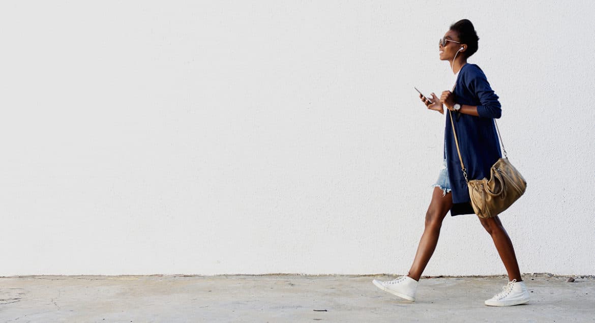 A woman finding stress relief while walking down a street with a cell phone in hand.