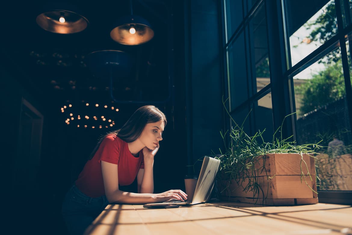 A woman engaging in remote work at a table using a laptop computer.