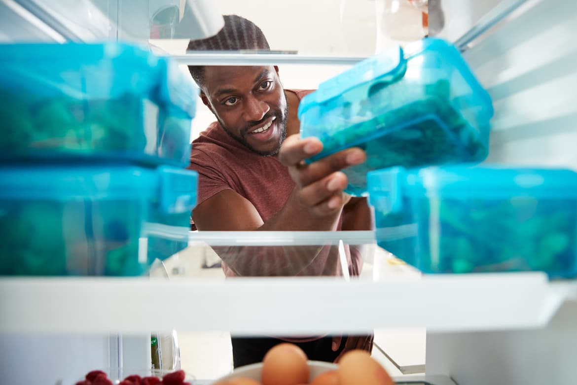 a man holding a bottle of water in a refrigerator.