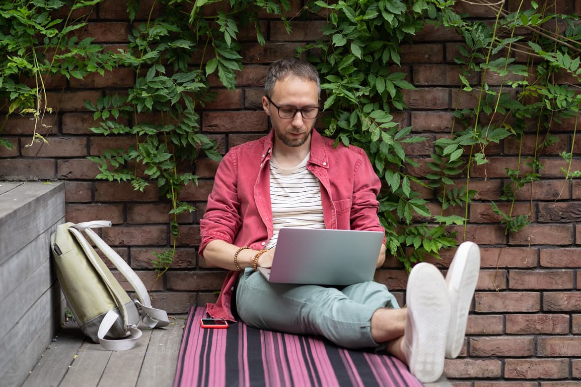 a man sitting on a bench using a laptop computer.