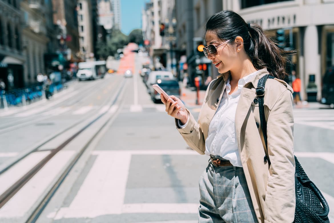 a woman standing on a street looking at her cell phone.