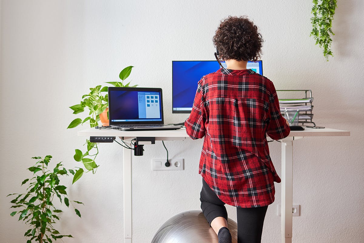 A woman working on two computers at a standing desk.