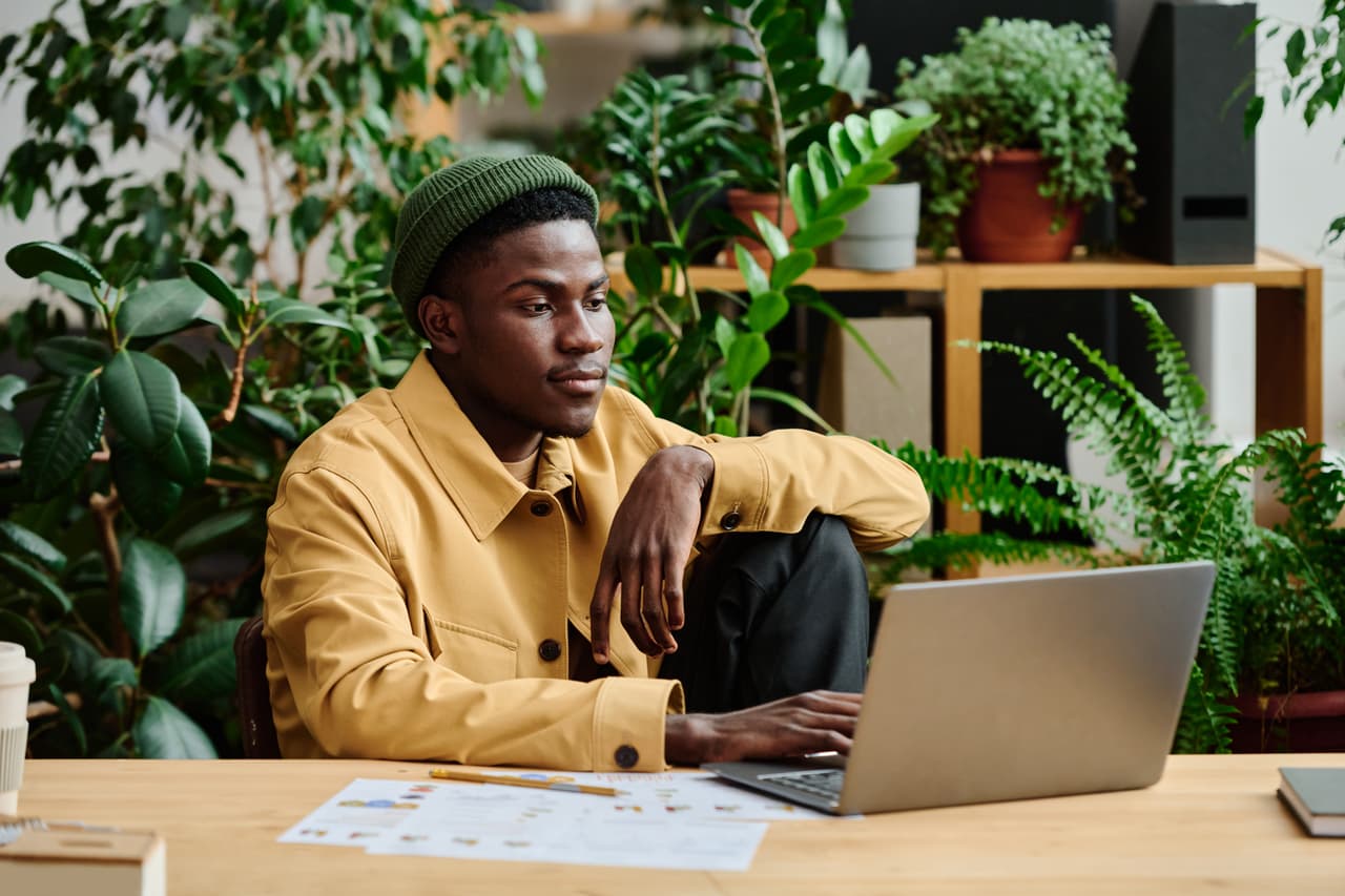 A digital nomad sitting at a desk with plants and a laptop.