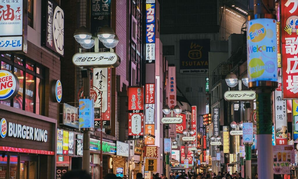 Colorful neon-lit street in Tokyo's busy Shibuya district, crowded with people and shops.