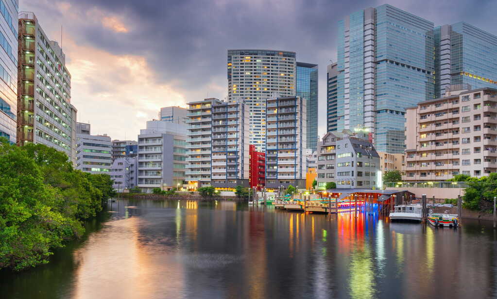 Apartment buildings along a canal in Tokyo at dusk, with lit boats docked on the water